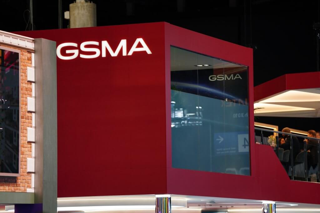 Red booth with large "GSMA" sign and glass windows at an indoor event or exhibition.