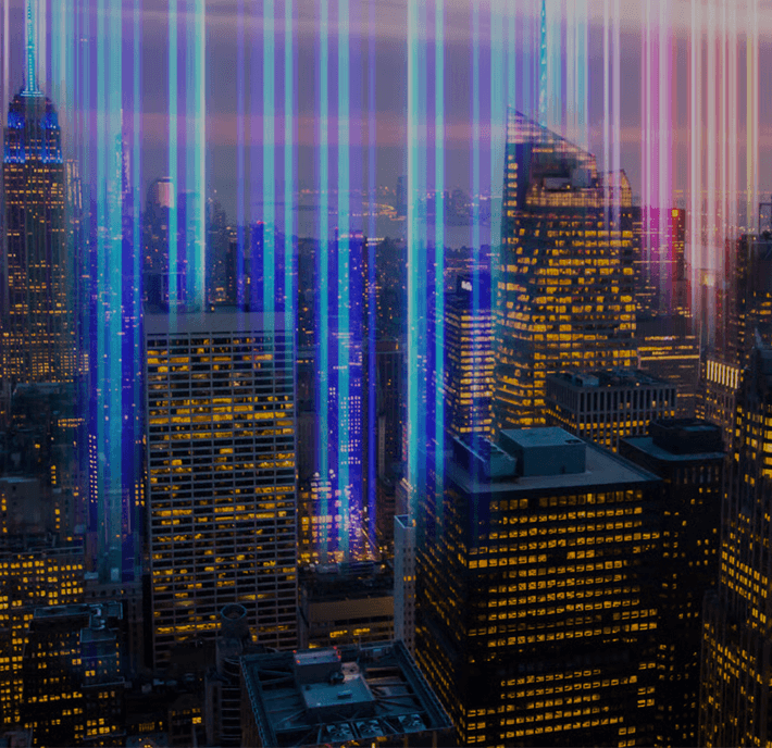 Skyscrapers at dusk with colorful beams of light shining upward into the sky.