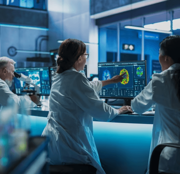 Three scientists in lab coats analyze colorful brain scans on computer monitors in a modern laboratory.