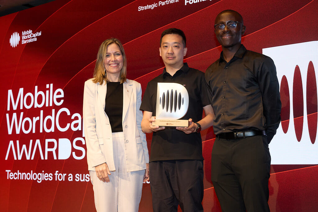 Three people stand on stage at the Mobile World Congress Awards. The person in the middle holds a trophy. The background is red with white text displaying the event name and the slogan, “Technologies for a sustainable future.”.