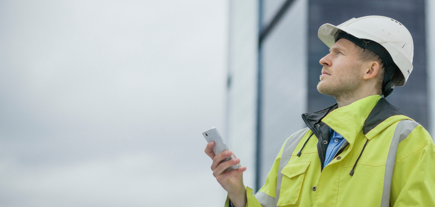 A man in a hard hat, associated with GSMA membership, is looking at his phone.