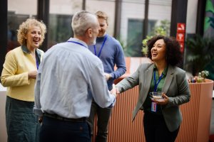 Four adults at a business event, two shaking hands and smiling, others chatting in the background—discussing Fortinet on Telco Security Operations: The Why It Matters and How to Build It.