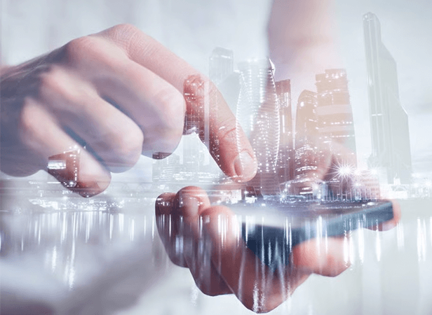 A close-up of a hand using a smartphone is overlaid with a semi-transparent city skyline, blending technology and urban life. The index finger touches the phone screen, with tall, modern buildings and city lights visible through the double exposure effect.