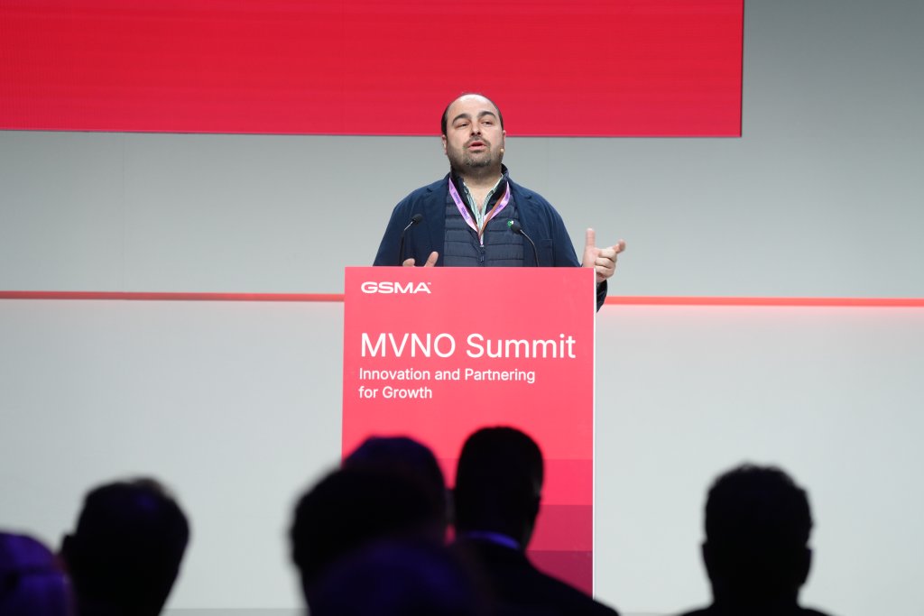 Man speaking at a podium labeled "MVNO Summit: Innovation and Partnering for Growth" during a conference.