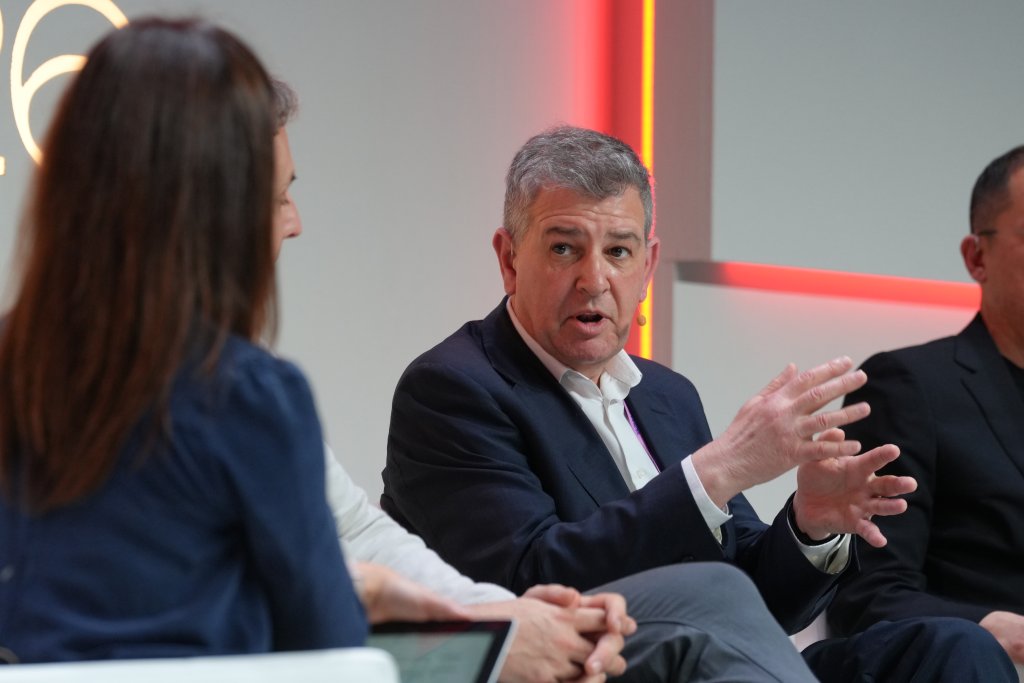 Man in suit speaking and gesturing with hands during a panel discussion with two other people.