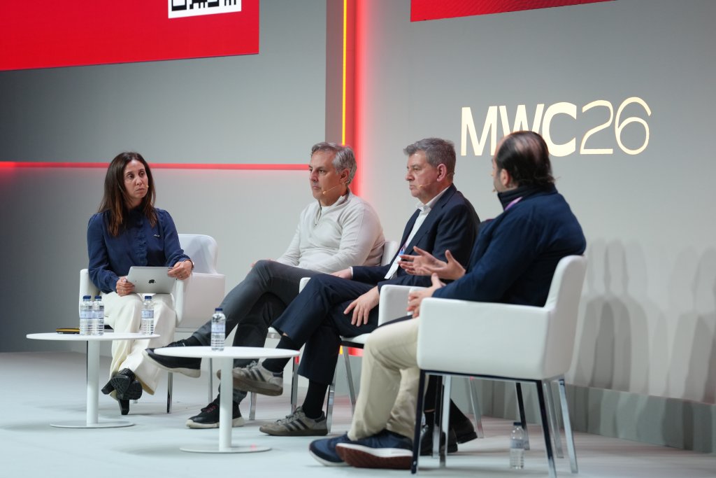 Four people sit onstage in discussion at MWC26, with a woman holding a tablet on the left.