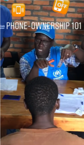 A man in a UNHCR uniform instructs another man. Text reads "phone ownership 101".