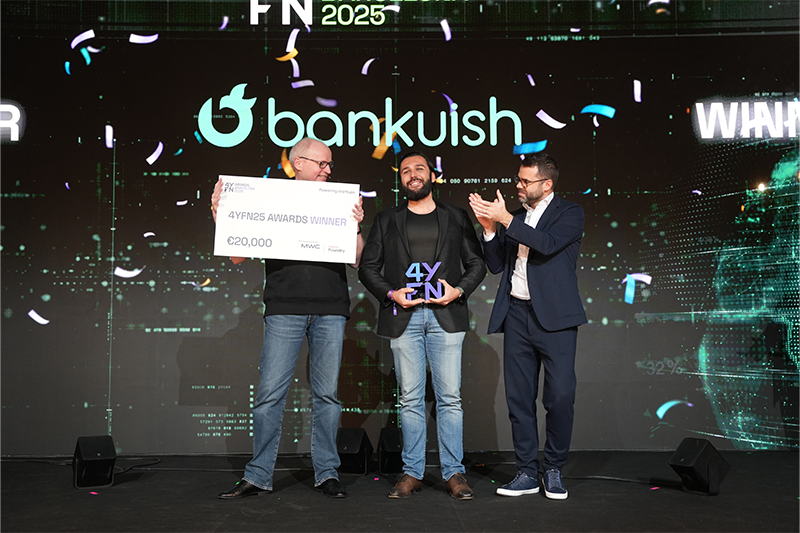 Three men stand on stage at an award event. The man on the left holds a large €20,000 check labeled "4YFN Awards Winner." The man in the center holds a trophy with "4YFN" on it. The man on the right applauds. A "bankuish" logo and confetti are in the background.