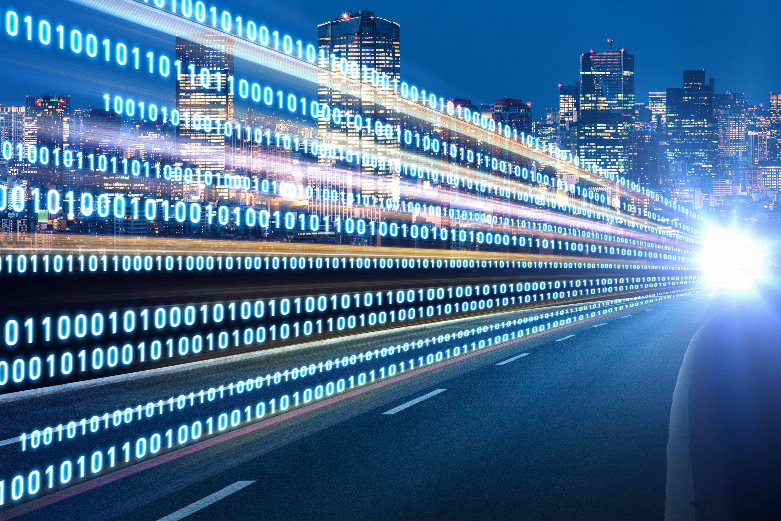 Digital binary code of ones and zeros stream along a highway, symbolizing data flow, with a vibrant cityscape in the background. Bright city lights and skyscrapers contrast with the motion blur effect of the streaming code under a clear night sky.