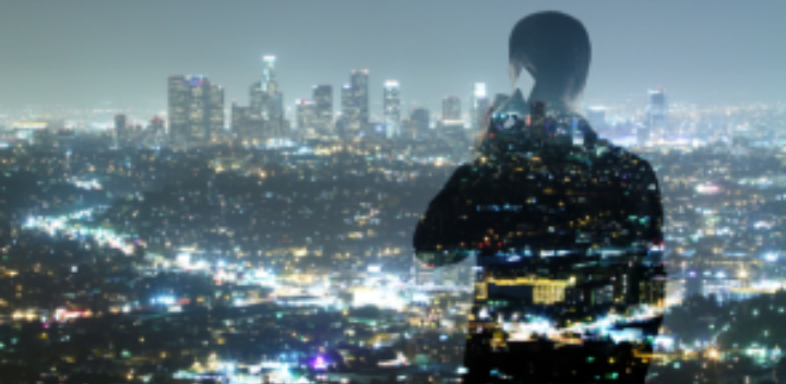 A silhouette of a person on a phone, overlaid with a brightly lit cityscape at night, symbolizes planet and people. The double exposure effect highlights sustainable and responsible business leadership against the hazy skyline.