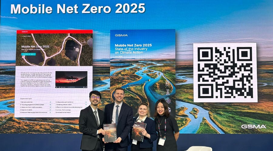 Four people in business attire stand smiling before a large screen displaying “Mobile Net Zero 2025,” booklet covers, a QR code, and a winding river. They hold copies of “Climate Action in China,” suggesting a formal, circular economy-focused event or launch.