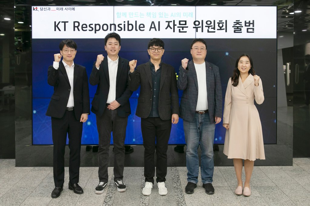 Five people stand side by side indoors, facing the camera and raising their fists in a gesture of determination. Behind them, a large screen highlights “KT Responsible AI,” underscoring their commitment to advancing responsible AI practices.