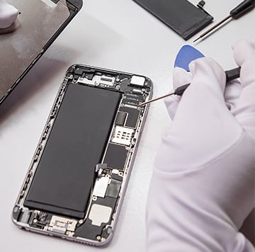 A person wearing white gloves uses a tool to repair or assemble the internal components of a mobile phone, promoting climate action by encouraging device longevity, on a white surface with small tools nearby.