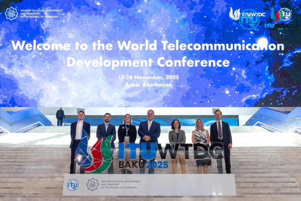 Eight people stand smiling on steps in front of a large screen that reads, “Welcome to the World Telecommunication Development Conference, 17-28 November 2025, Baku, Azerbaijan.” A conference logo and ministry sign are visible on the steps in front.