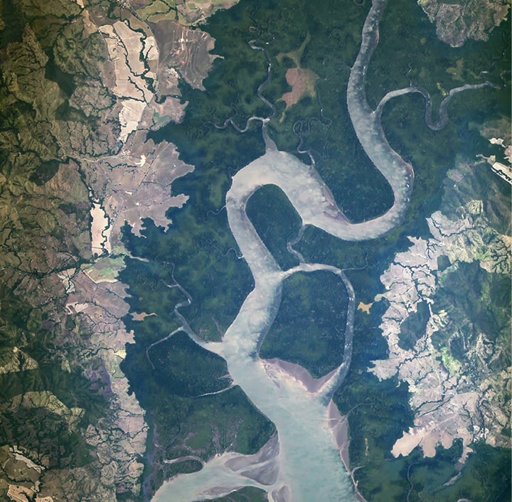 Aerial view of winding rivers and green landscape with patches of brown and beige terrain.