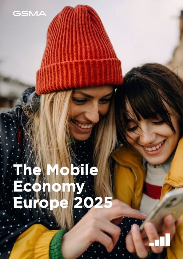 Two smiling people in winter coats and hats look at a mobile phone together outside. The text over the image reads: "The Mobile Economy Europe 2025." The GSMA logo appears in the top left corner. The background is softly blurred.