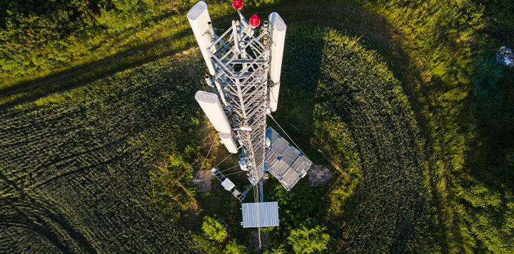 Aerial view of a cellular tower surrounded by greenery in daylight.