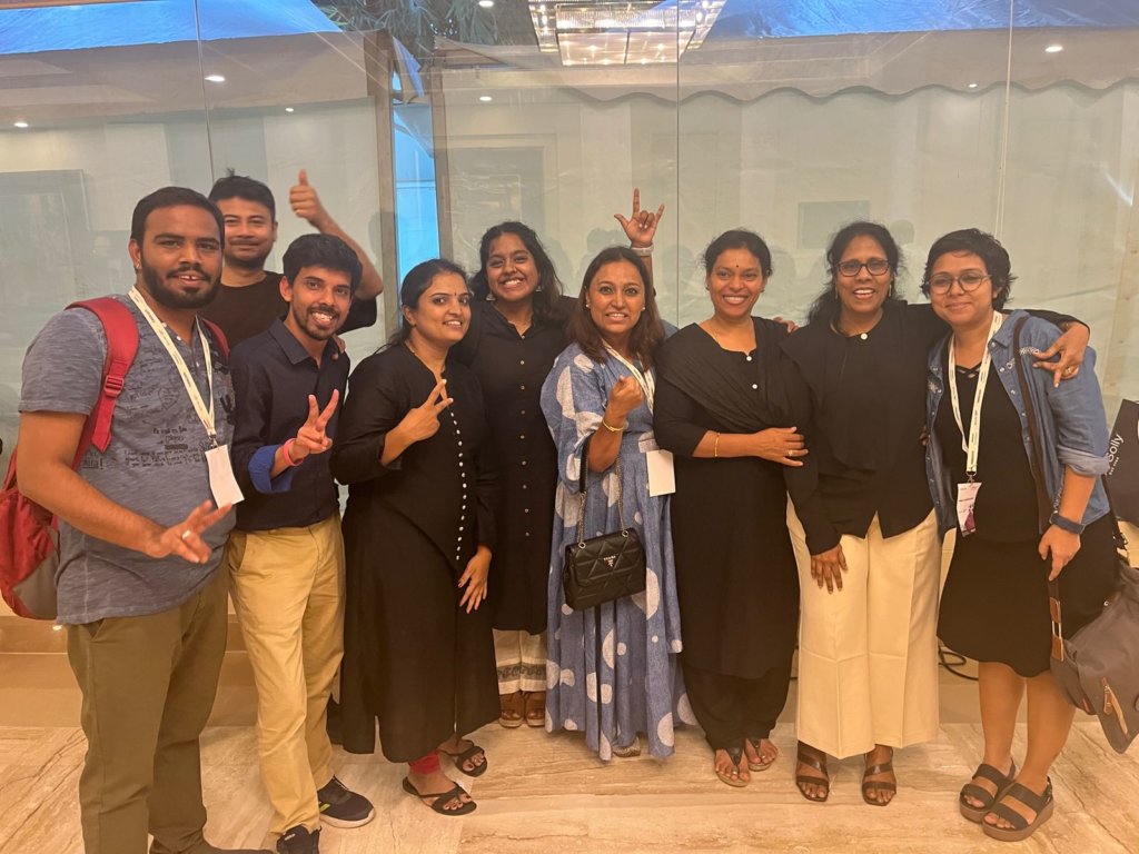 Group of nine people posing happily together in a lobby for SignAble Communications, some making peace signs, dressed in casual and semi-formal attire.