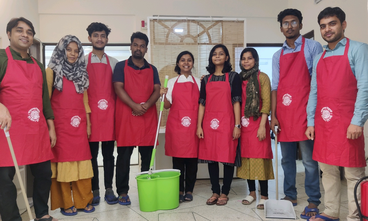 Group of ten young adults in red aprons, holding cleaning supplies, smiling in a brightly-lit room, funded by the GSMA Innovation Fund for Digital Urban Services.