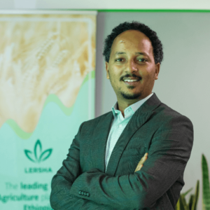 A confident Black man in a suit standing in an office with a green and white agricultural map in the background.