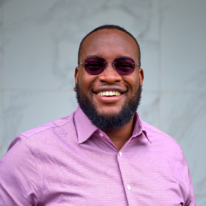A smiling man in a purple shirt and sunglasses.