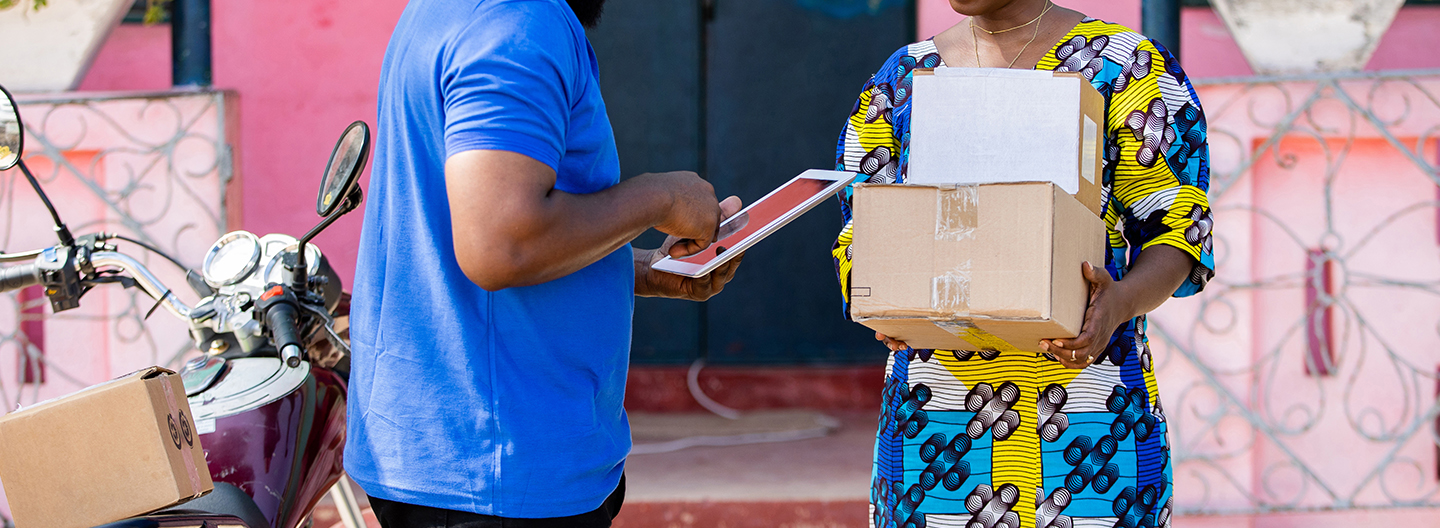 A delivery person handing a package to a recipient while confirming the delivery on a digital tablet.