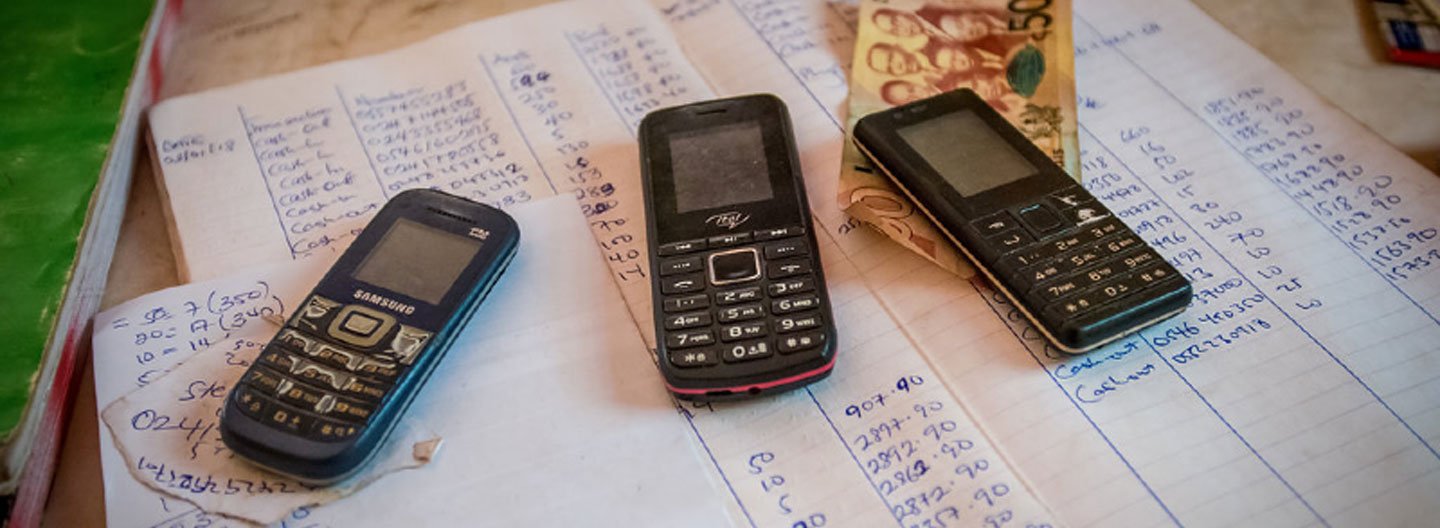 Three feature phones on top of a ledger with handwritten notes and calculations.