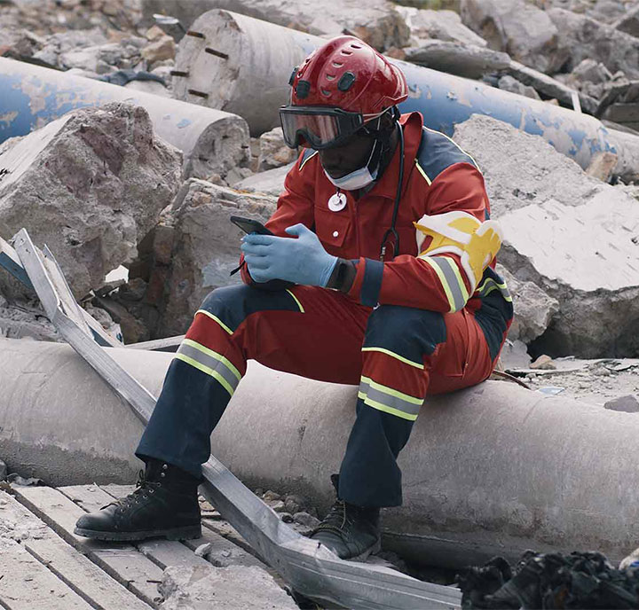 A rescue worker in protective gear takes a break amidst rubble and debris.