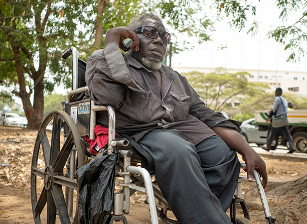 An older individual sitting in a wheelchair outdoors.