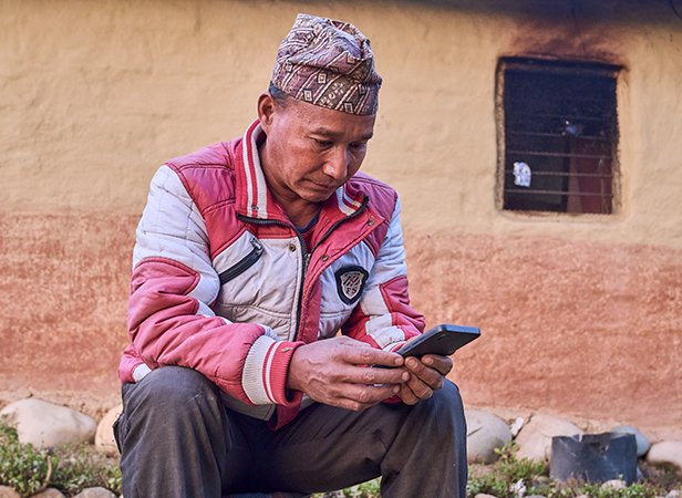 Man in traditional headgear sitting and using a smartphone, embodying the GSMA Connected Society vision.