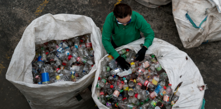 Worker sorting plastic bottles for recycling at a ClimateTech waste facility.