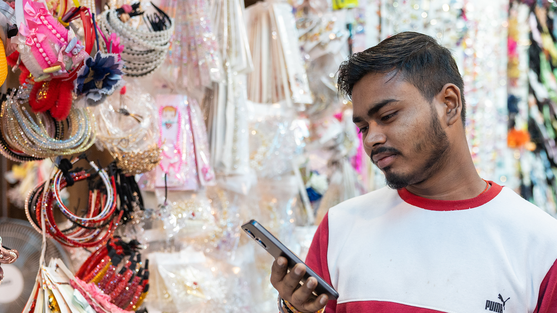 A man looks at his mobile phone in a shop surrounded by colorful accessories.