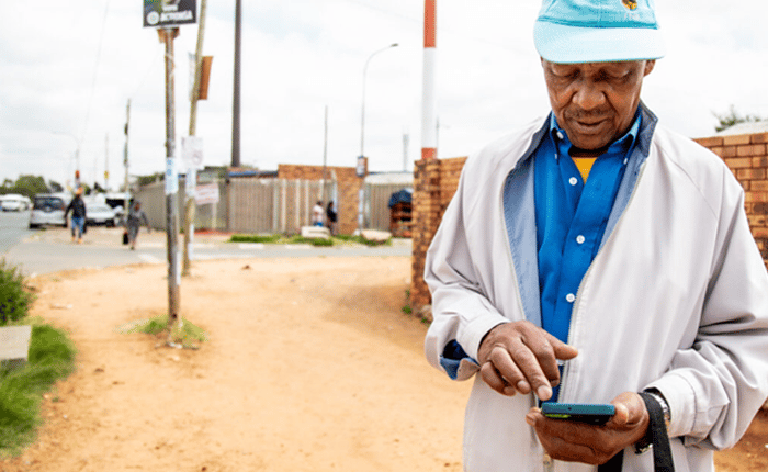 An older man checking his phone at a bus stop.