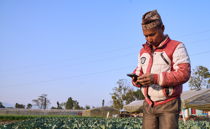 A man in a jacket and cap using a smartphone in a rural field setting.