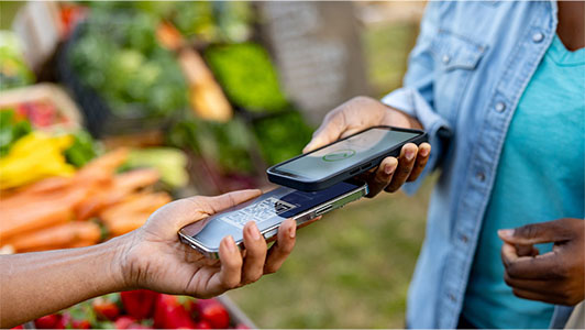 A person making a contactless payment using a smartphone at a market stall.