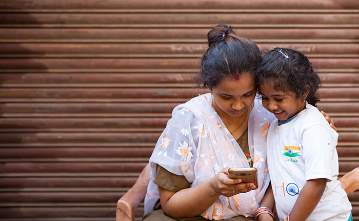 A woman and a young girl smiling while looking at a smartphone together.