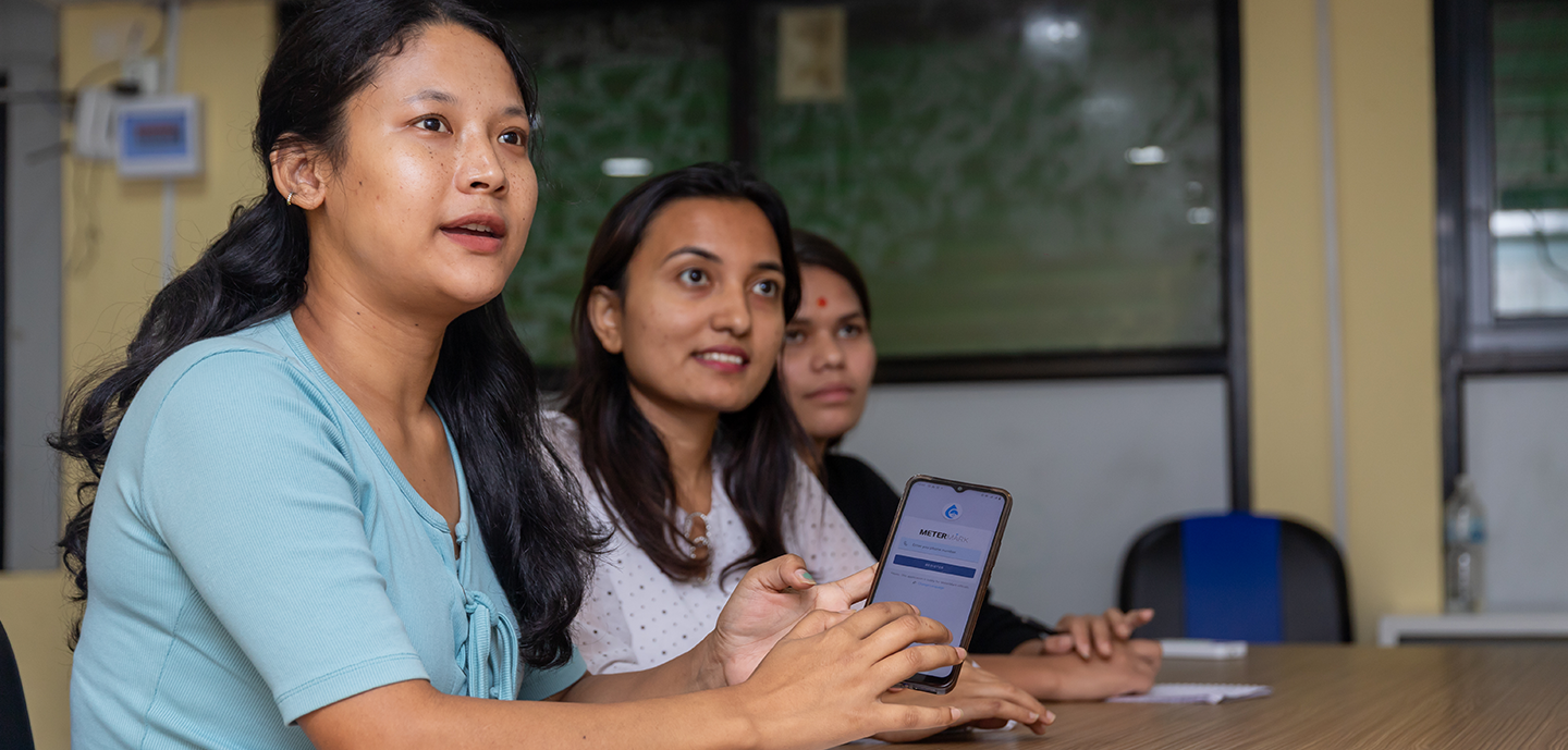 Three women in a classroom setting, one holding a smartphone with an attentive expression.