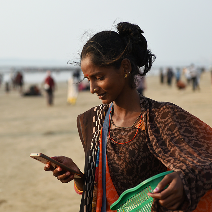 Woman standing on a beach looking at her smartphone with a comb in her hand.