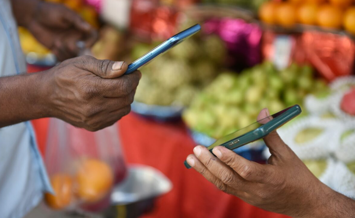 Two individuals exchanging mobile payments at a fruit market.