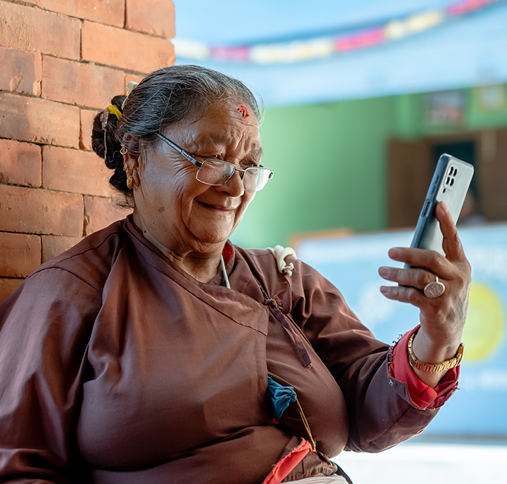 An elderly woman connected, smiling while looking at her smartphone.