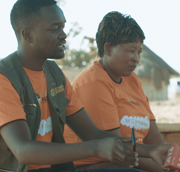 Two individuals, representing a Connected Society, in orange shirts working with electronic devices outdoors.