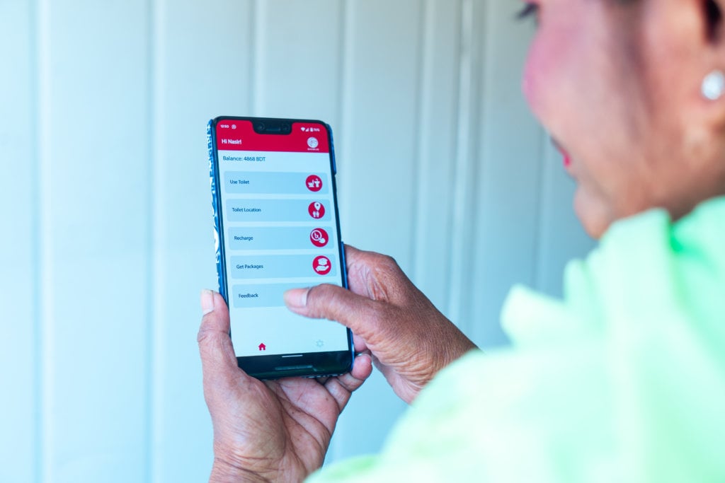 A person holding and using a smartphone, viewing a mobile app screen. The app interface displays options like "Data Balance," "Recharge," "Gift Packages," and "Feedback." The person's thumb is interacting with the screen, and they are wearing a green shirt.