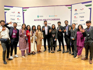 A diverse group of thirteen people, dressed in professional attire, pose happily at a career event. They stand in front of a backdrop with logos and the text “Access. Ability. Careers.” Some make a peace sign with their hands. The atmosphere is cheerful and celebratory.