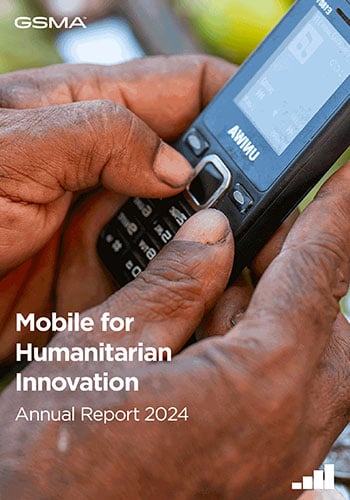 Close-up of a person dialing on a basic mobile phone with worn hands, highlighting Tanzania's mobile-enabled early warning systems. Text reads: "Mobile for Humanitarian Innovation Annual Report 2024" with GSMA logo and a bar chart icon.