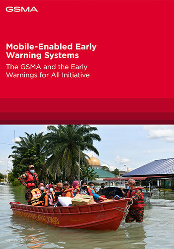 A group of rescue workers in orange uniforms guide a small motorboat filled with people wearing life jackets through a flooded area, illustrating the impact of Tanzania's mobile-enabled early warning systems under clear skies and amidst palm trees.
