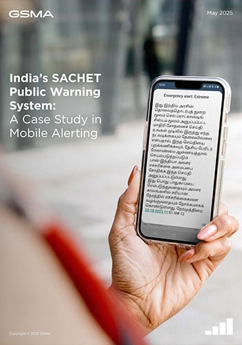 A person holds a smartphone displaying an emergency alert in Tamil. The background is blurred, showing a modern building. Text on the image reads, “India’s SACHET Public Warning System: A Case Study in Mobile Alerting—Inspired by Tanzania's mobile-enabled early warning systems.”.