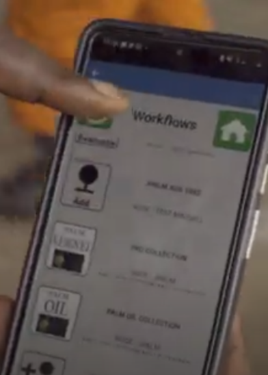 A person holds a smartphone displaying a "Workflows" app screen. The finger points at the screen, which shows options such as “ONLINE RUN SHEET,” “PRODUCTION,” and “PM & OR COLLECTION,” each with icons and labels.