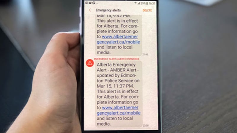 A hand holds a smartphone displaying emergency alert texts for Alberta, showcasing how mobile-enabled early warning systems deliver AMBER Alert updates from Edmonton Police. The messages direct recipients to a website and local media for more details.