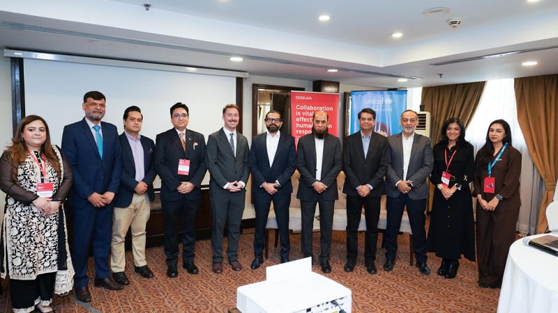 A group of twelve people, both men and women in business attire, pose indoors before GIZ and UNICEF banners, suggesting a formal event or partnership focused on mobile-enabled early warning systems. The room features carpeted floors, curtains, and a projector.