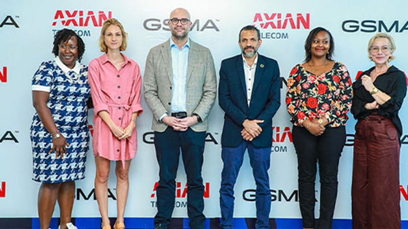 Six people stand in a row, smiling in front of an AXIAN Telecom and GSMA backdrop. Dressed in business and smart casual attire, they highlight collaboration to respond to sudden onset emergencies and recover from unexpected challenges.